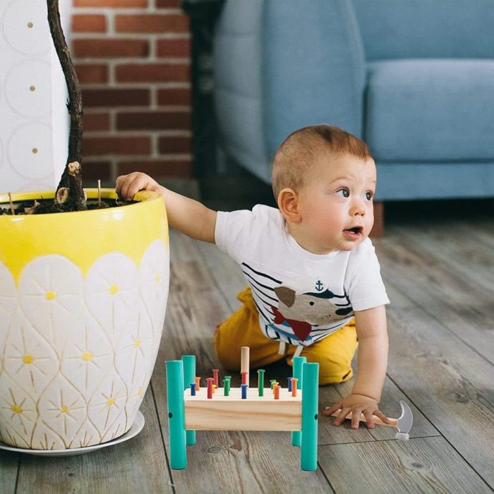 Un bébé joue avec un xylophone en bois dans un salon, tout en s'amusant avec le Jeu de Construction Clou-Marteau.
